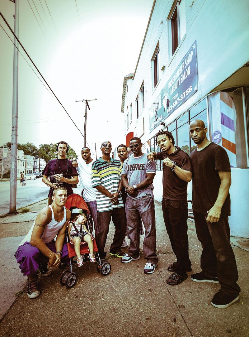 Locals pose for a group portrait with Henkin (in headphones) and Patrick (far right) outside Diamond Cutz on East Patapsco Avenue. Patrick often sets his camera on a timer to capture these moments.