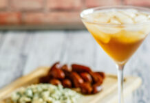 A Crowd-Pleasing and Simple Holiday Appetizer Photo of a plate of bacon-wrapped dates, each stuck with toothpick, in front of a cocktail.