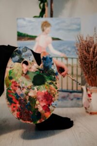 A person with a paint palette sits in front of an impressionist painting